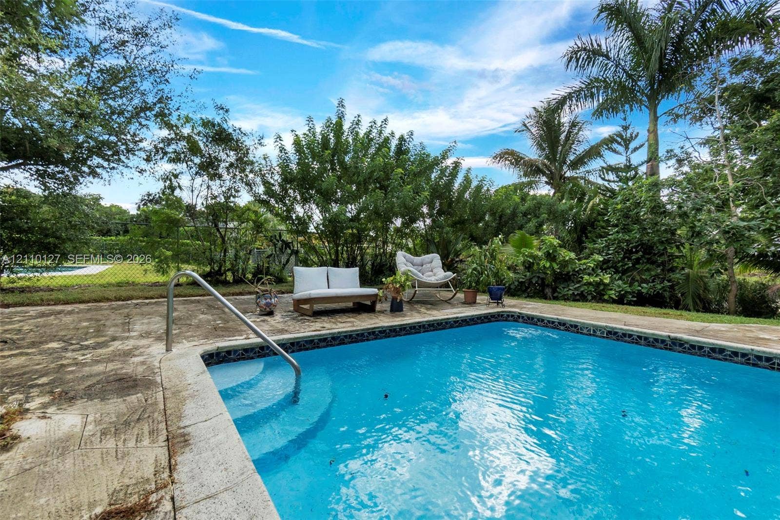 10164 SW 52nd Street, Cooper City, FL 33328 In-ground pool featuring a metal handrail, concrete patio surround, mature trees, and perimeter fencing