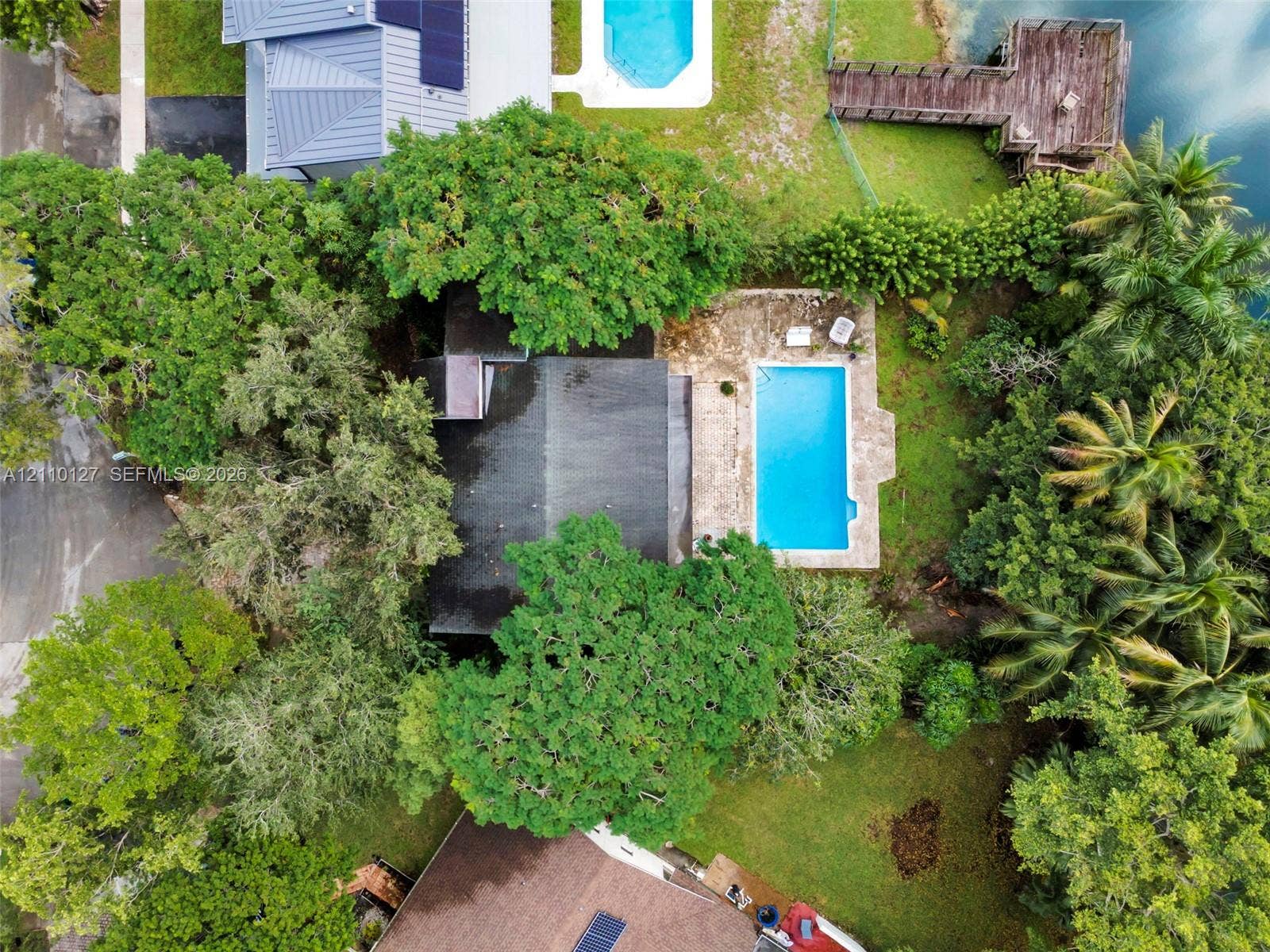 10164 SW 52nd Street, Cooper City, FL 33328 Aerial perspective featuring a private swimming pool, stone patio, wooden dock, and mature canopy trees on a waterfront lot