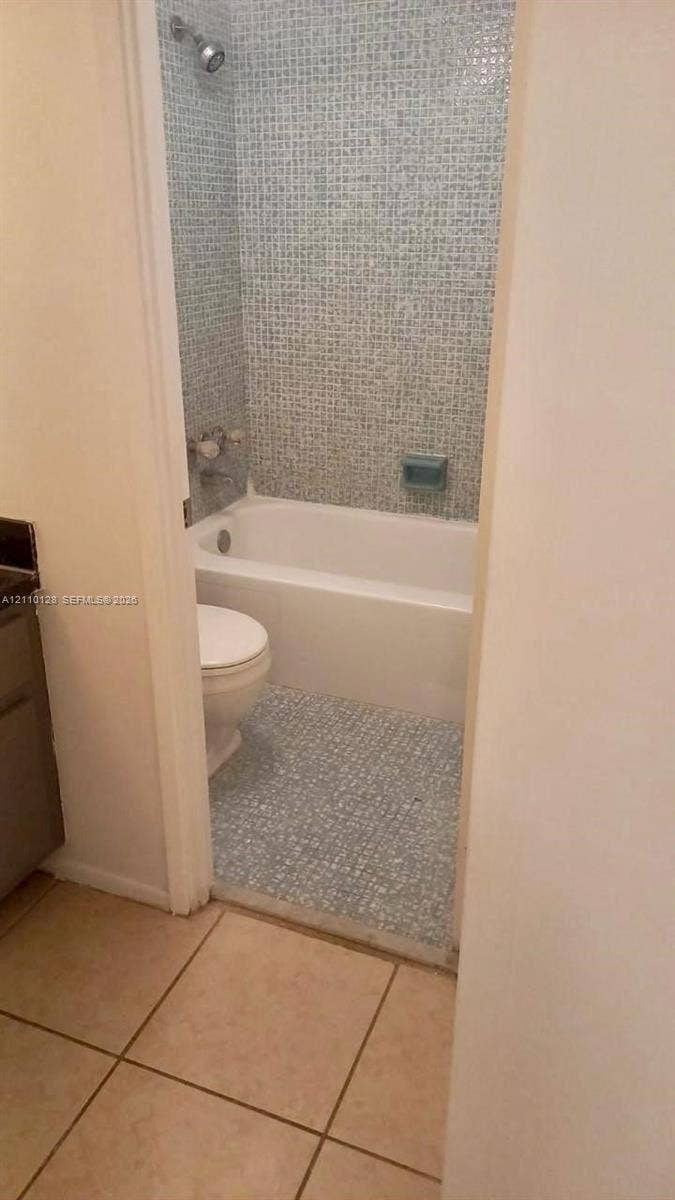 1351 NE Miami Gardens Drive, #1624E, Miami, FL 33179 Bathroom featuring blue mosaic wall tile, a white porcelain soaking tub, a built-in soap niche, and light-toned floor tiling