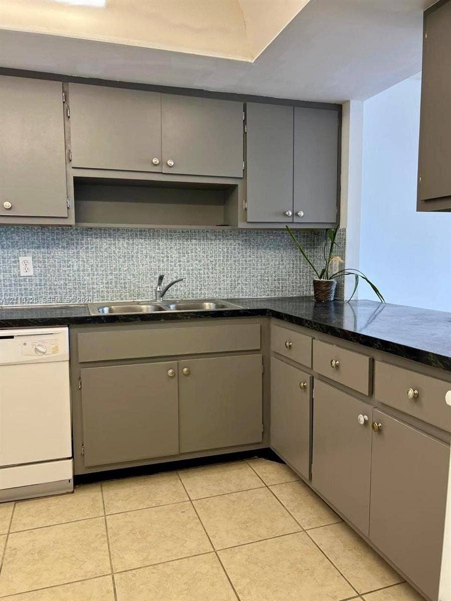1351 NE Miami Gardens Drive, #1624E, Miami, FL 33179 Kitchen featuring gray cabinetry, dark countertops, patterned tile backsplash, dual-basin stainless steel sink, and ceramic tile flooring