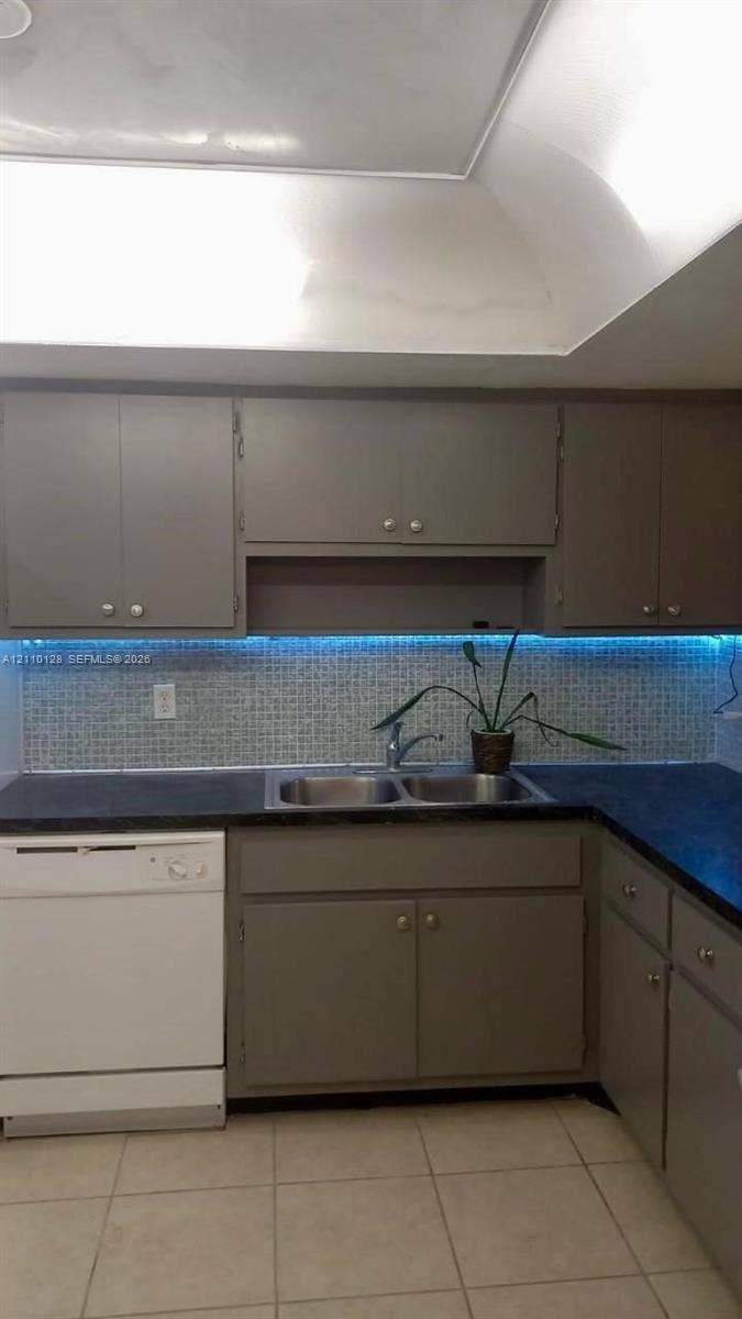 1351 NE Miami Gardens Drive, #1624E, Miami, FL 33179 Kitchen featuring painted cabinetry, dark solid-surface countertops, mosaic tile backsplash, integrated under-cabinet lighting, and a stainless steel double-basin sink