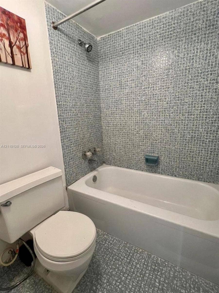 1351 NE Miami Gardens Drive, #1624E, Miami, FL 33179 Bathroom featuring a porcelain bathtub, integrated shower fixture with curtain rod, patterned mosaic wall tiling, and a built-in soap dish