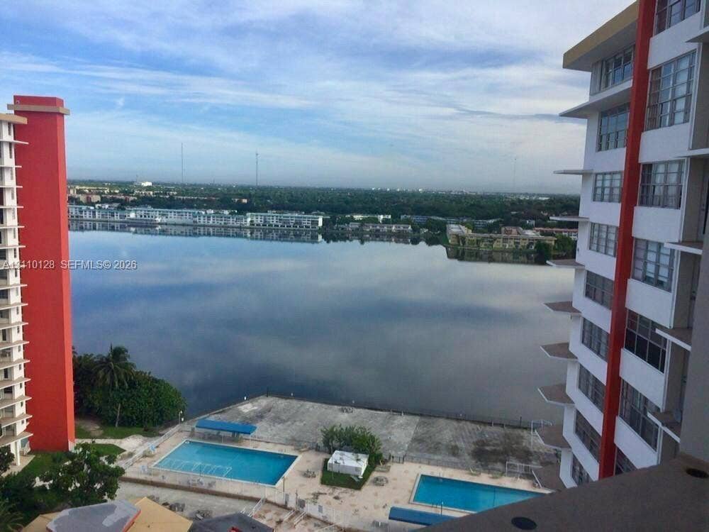 1351 NE Miami Gardens Drive, #1624E, Miami, FL 33179 High-rise exterior with dual swimming pools and concrete pool deck, centered on a large lake expanse