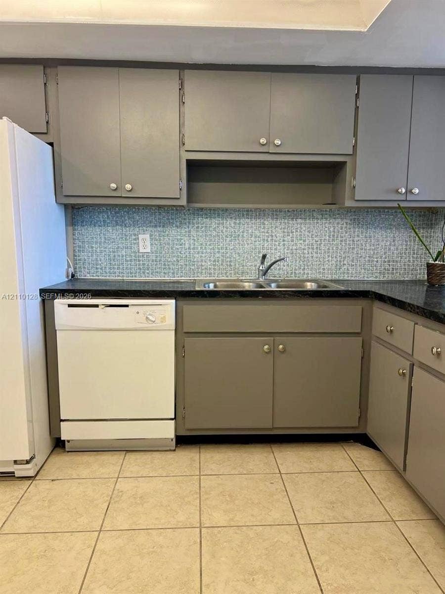 1351 NE Miami Gardens Drive, #1624E, Miami, FL 33179 Kitchen featuring gray cabinetry, dark solid-surface countertops, mosaic tile backsplash, double-basin stainless steel sink, and ceramic tile flooring