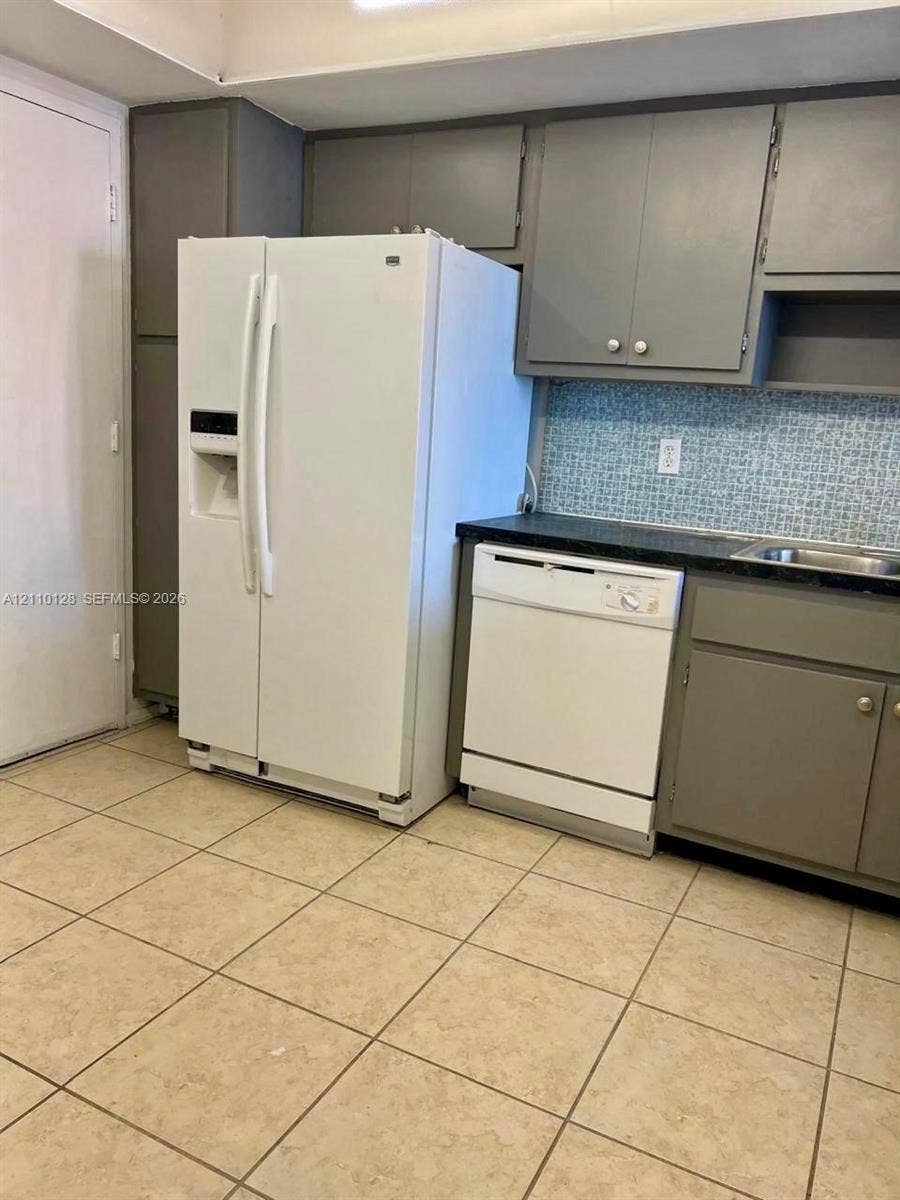 1351 NE Miami Gardens Drive, #1624E, Miami, FL 33179 Kitchen featuring grey cabinetry, dark solid-surface countertops, decorative mosaic tile backsplash, ceramic tile flooring, and integrated appliances
