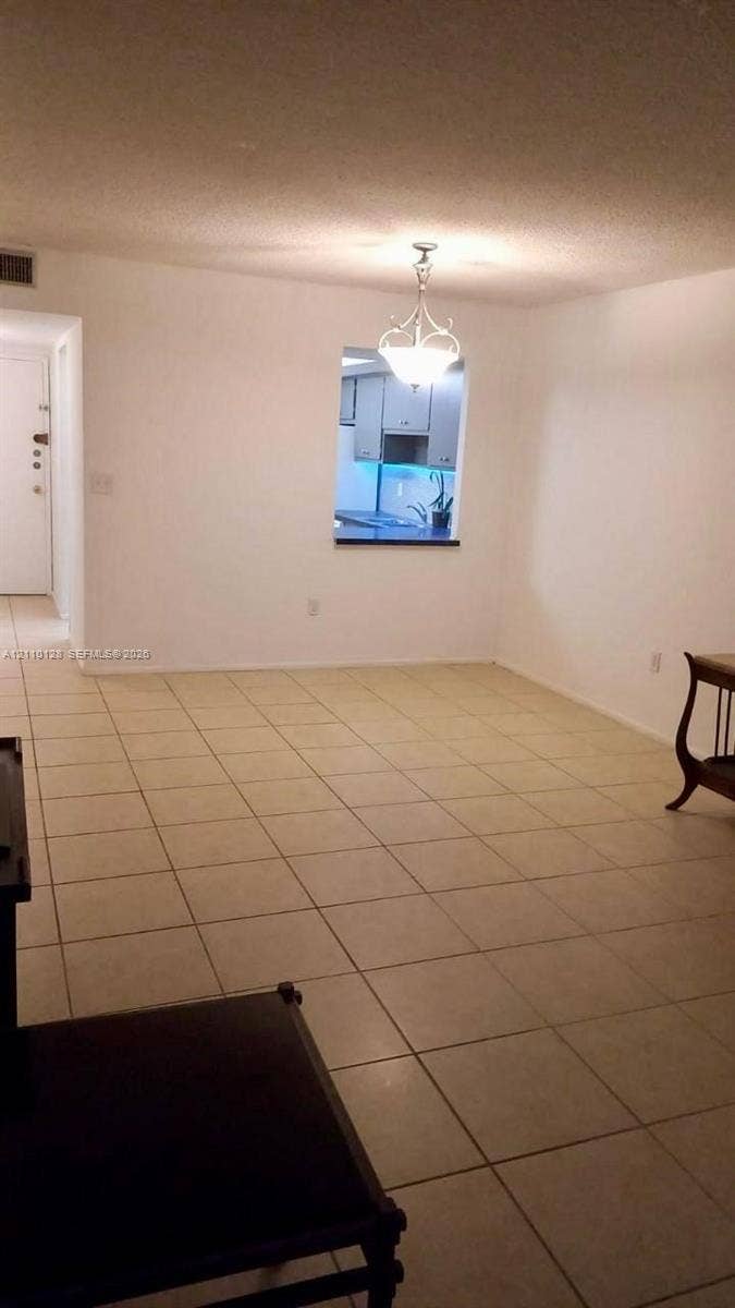 1351 NE Miami Gardens Drive, #1624E, Miami, FL 33179 Open-concept space featuring neutral tile flooring, a decorative chandelier, and a kitchen pass-through window with a countertop ledge