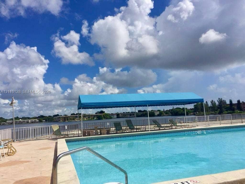 1351 NE Miami Gardens Drive, #1624E, Miami, FL 33179 In-ground swimming pool featuring a metal safety railing, paved decking, and a blue fabric canopy structure