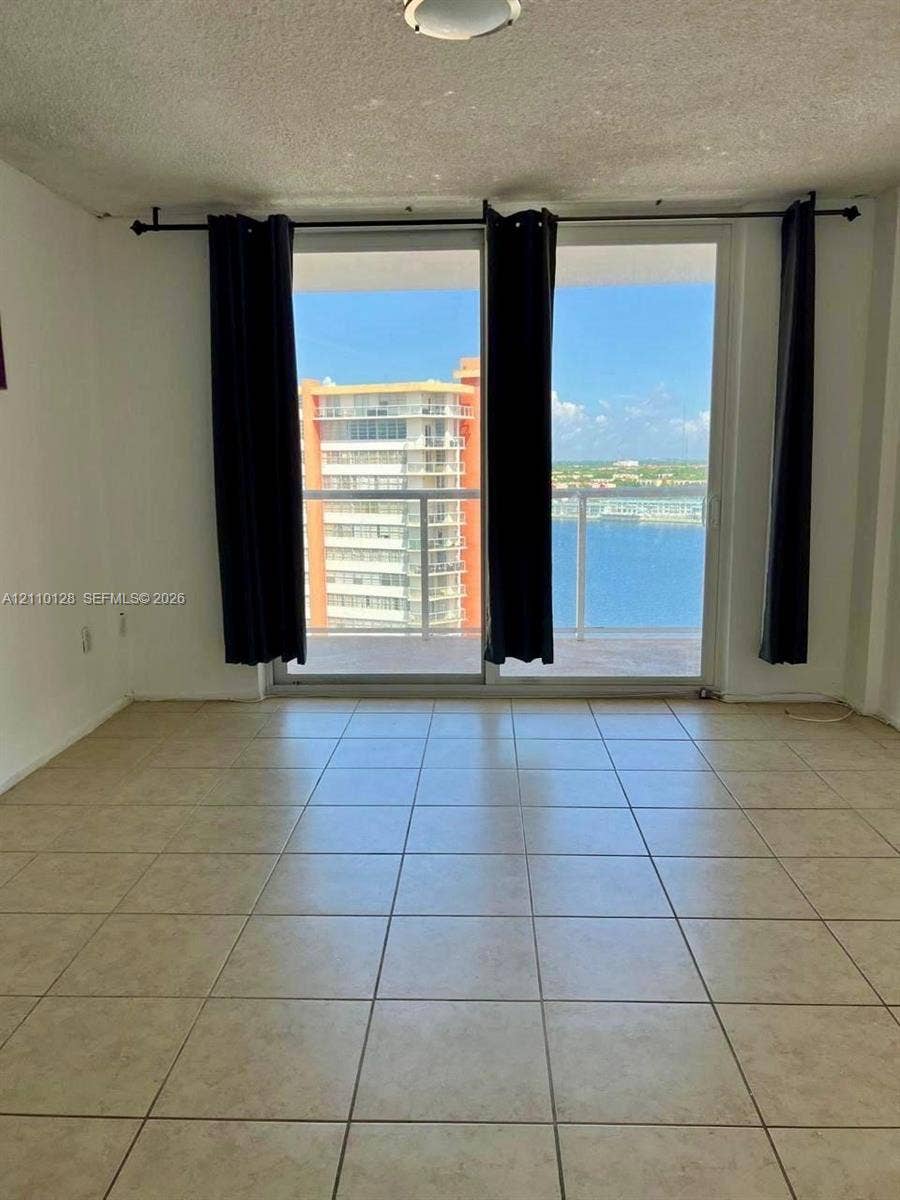 1351 NE Miami Gardens Drive, #1624E, Miami, FL 33179 Floor-to-ceiling sliding glass doors opening to a balcony with a glass railing and ceramic tile flooring