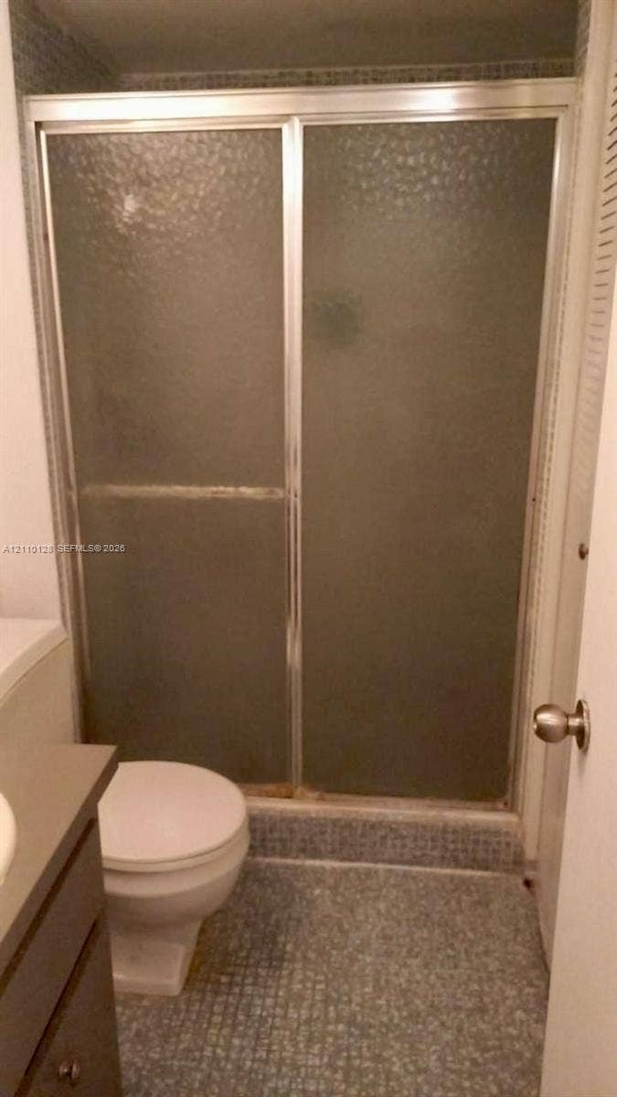 1351 NE Miami Gardens Drive, #1624E, Miami, FL 33179 Shower stall featuring a metal-framed enclosure with textured privacy glass and a tiled floor, accompanied by a built-in vanity cabinet and standard porcelain toilet
