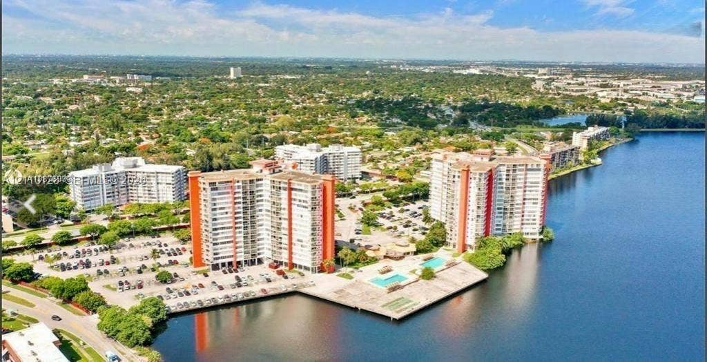 1351 NE Miami Gardens Drive, #1624E, Miami, FL 33179 Aerial perspective of a multi-story residential complex featuring waterfront access, paved surface parking, and a swimming pool