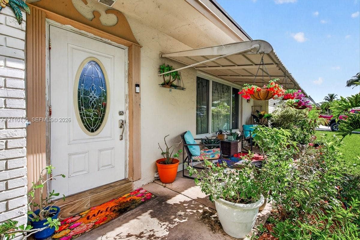 Entryway featuring a white door with an oval glass insert, decorative millwork trim, a concrete porch, and a metal window awning