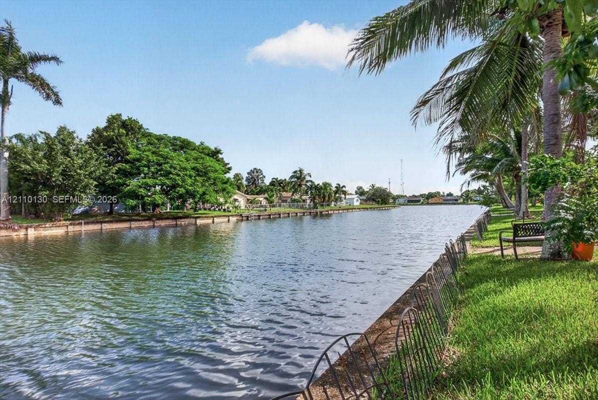 Waterfront property featuring a concrete seawall, expansive lawn, and mature palm trees