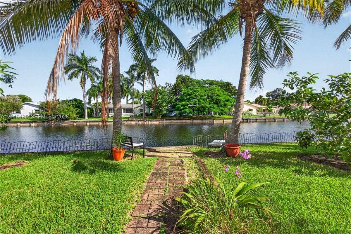 Waterfront backyard featuring a paver stone path, mature palm trees, decorative metal fencing, and manicured turf