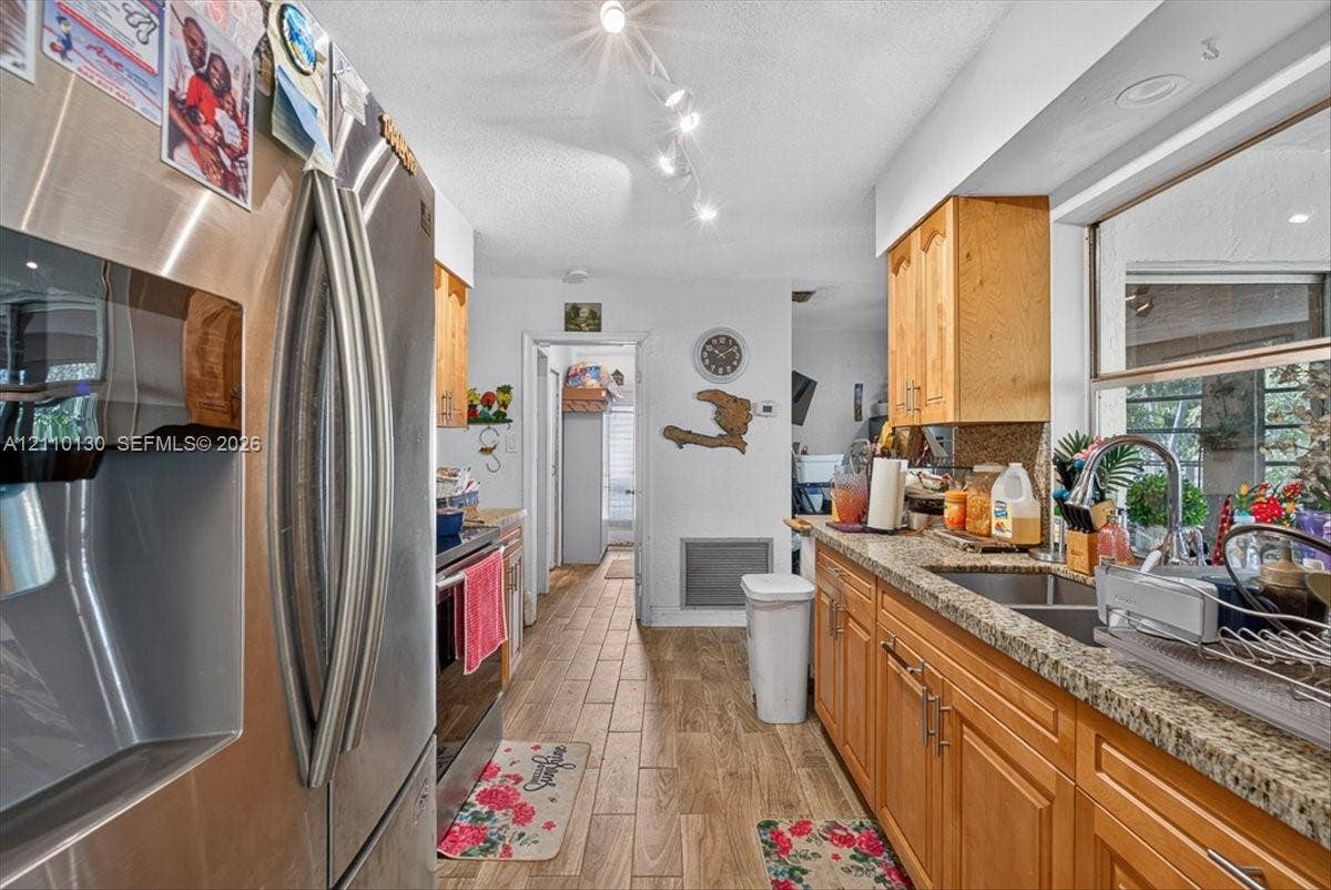 Kitchen featuring stainless steel refrigerator, stone countertops, double-basin undermount sink with gooseneck faucet, wood-finish cabinetry, and wood-finish flooring