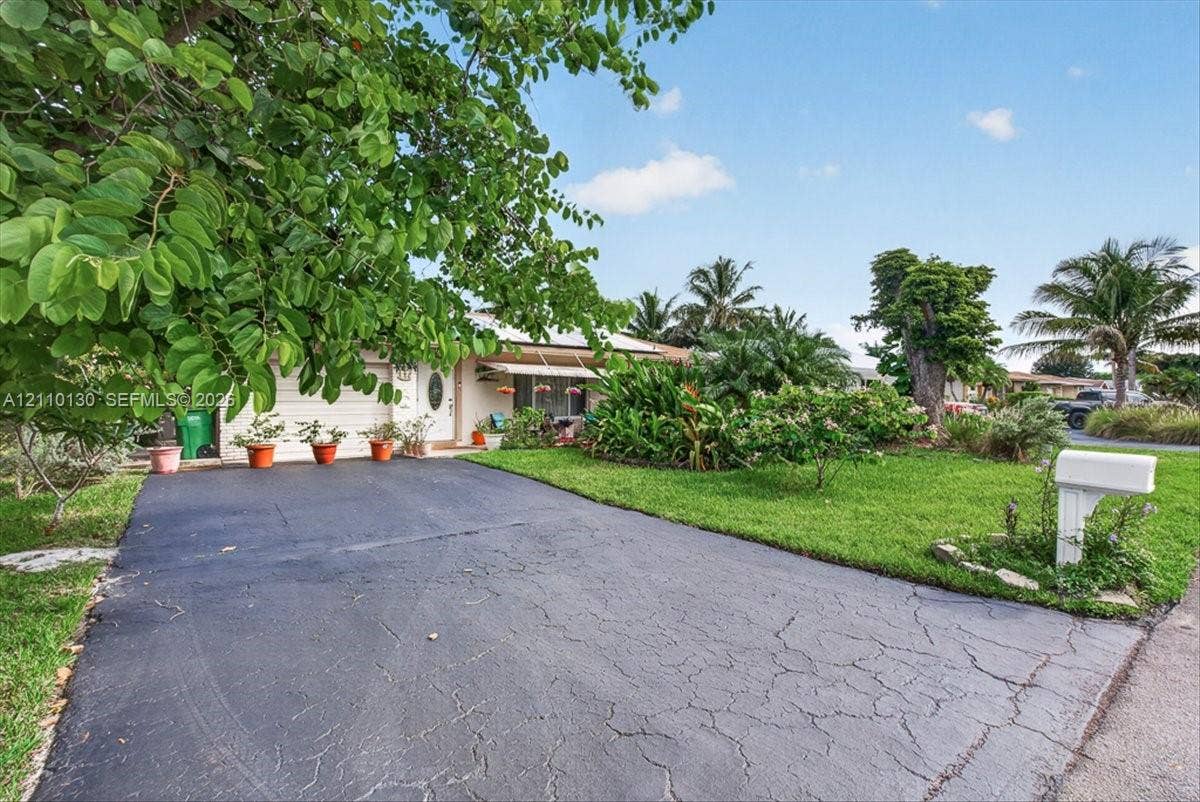 Asphalt driveway leading to a multi-car garage, complemented by established landscaping and mature trees