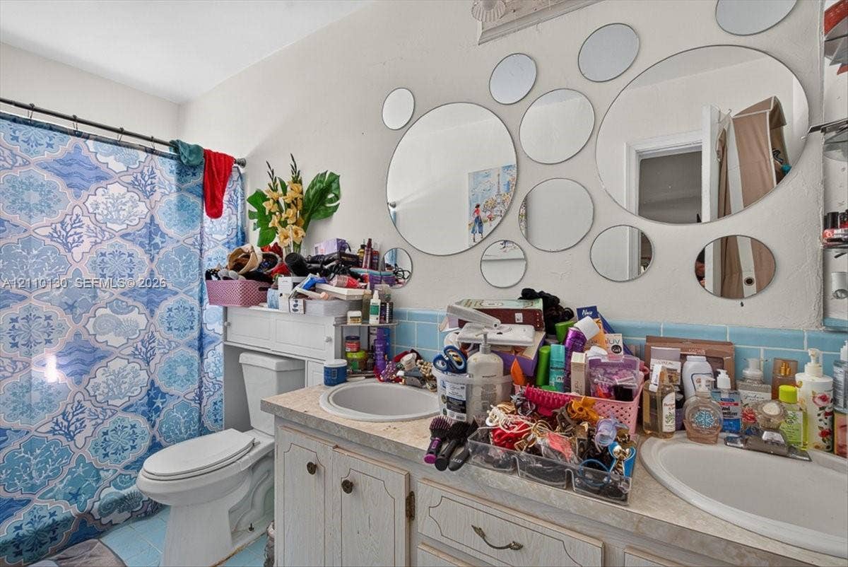 Bathroom featuring a double-sink vanity with white cabinetry and a light-toned countertop, paired with blue tile backsplash and a built-in toilet
