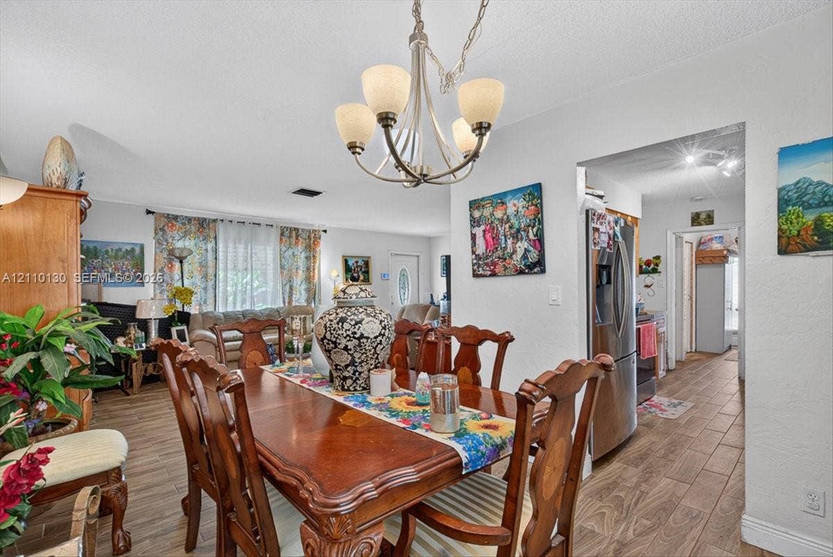 Wood-finish flooring throughout, multi-arm brushed metal chandelier, and stainless steel refrigerator