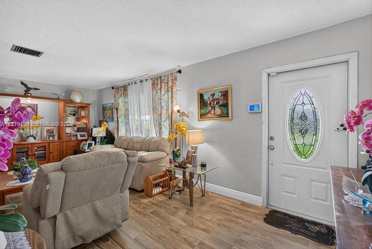 Living area featuring wood-finish flooring, built-in wooden shelving, and a white entry door with an oval decorative glass insert