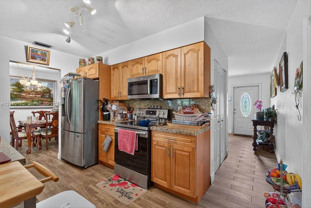 Kitchen featuring wood-finish cabinetry, stone-style countertops, stainless steel appliances, track lighting, and tile flooring