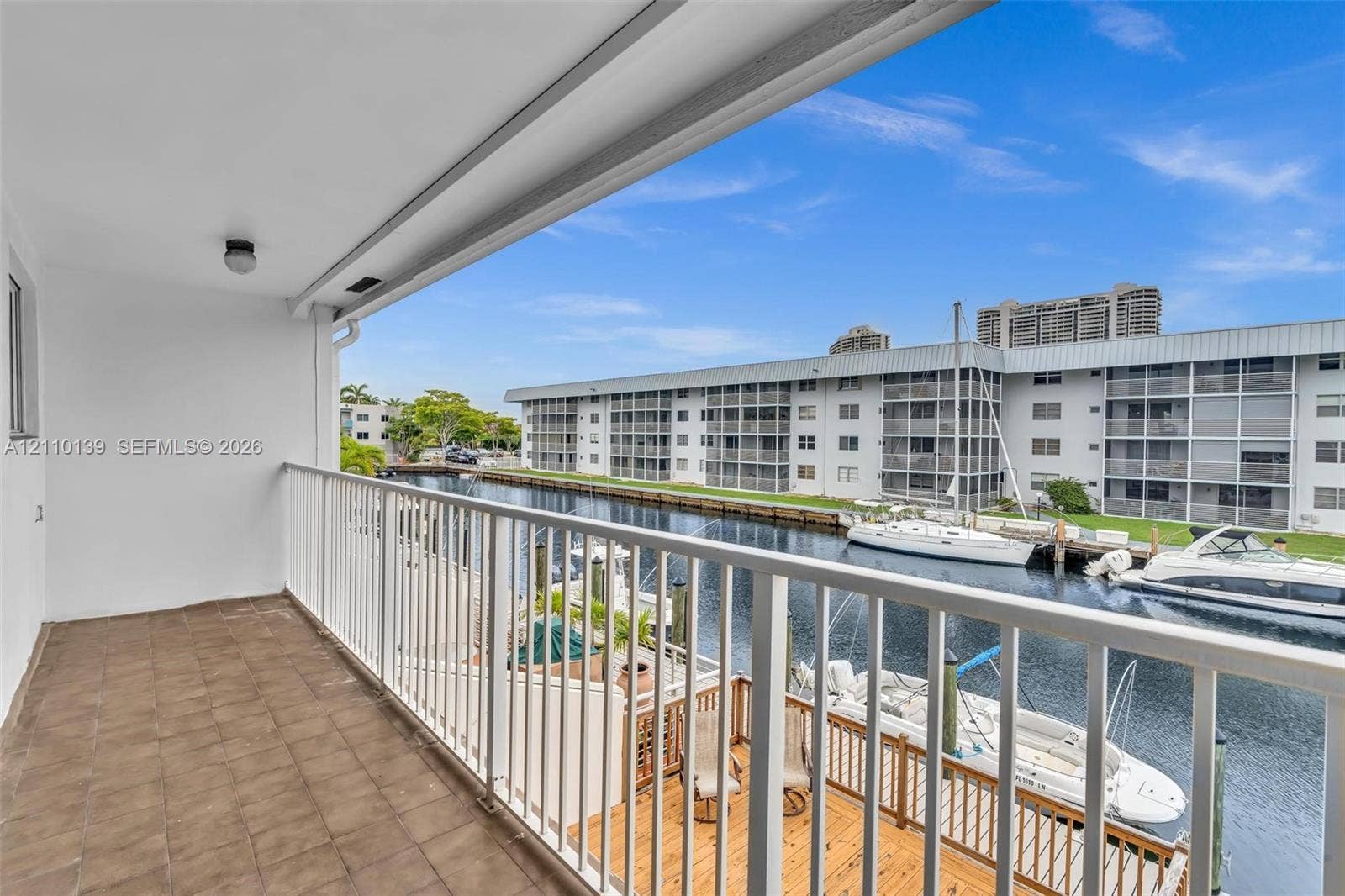 3601 NE 168th Street, #108, North Miami Beach, FL 33160 Covered balcony featuring tile flooring and metal railings, overlooking a canal with boat docking