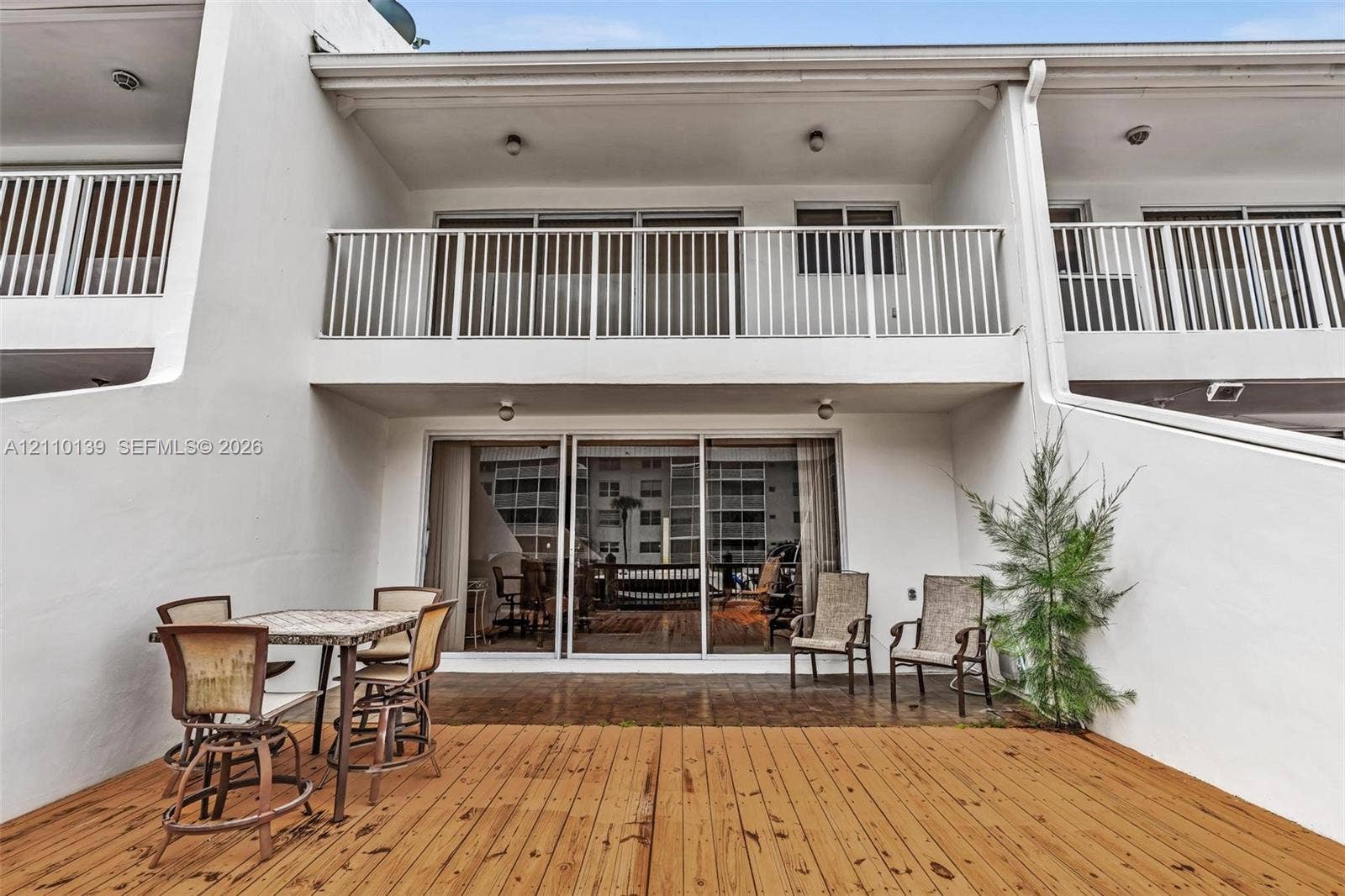 3601 NE 168th Street, #108, North Miami Beach, FL 33160 Exterior terrace featuring a wood-finish deck, sliding glass door entry, and second-story balcony with white metal railing