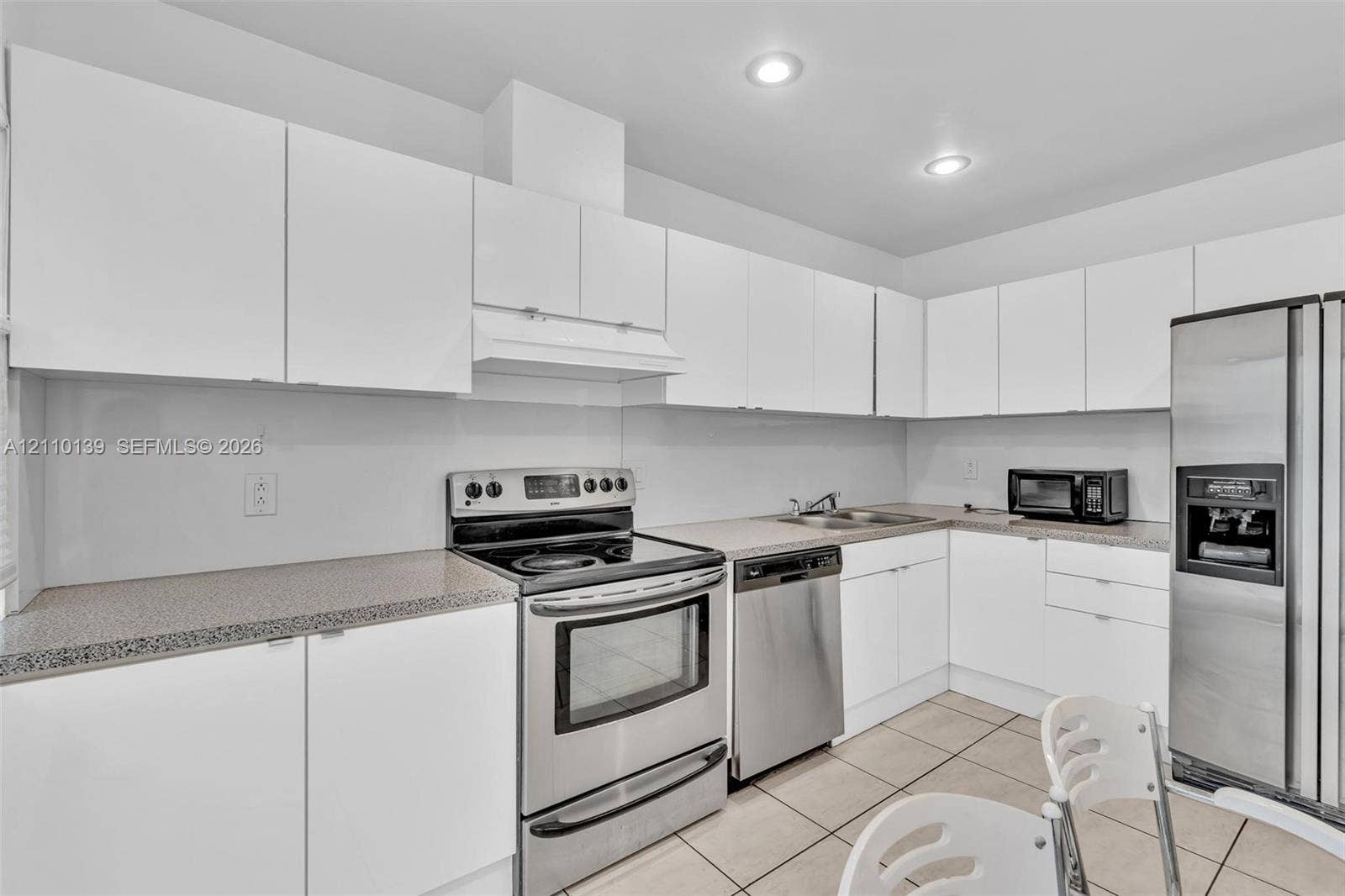 3601 NE 168th Street, #108, North Miami Beach, FL 33160 Kitchen featuring white flat-panel cabinetry, speckled stone-finish countertops, stainless steel appliances, and tiled flooring
