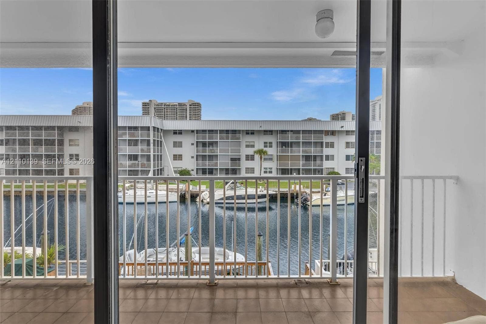 3601 NE 168th Street, #108, North Miami Beach, FL 33160 Covered balcony with neutral tile flooring, white metal railing, and sliding glass entry door