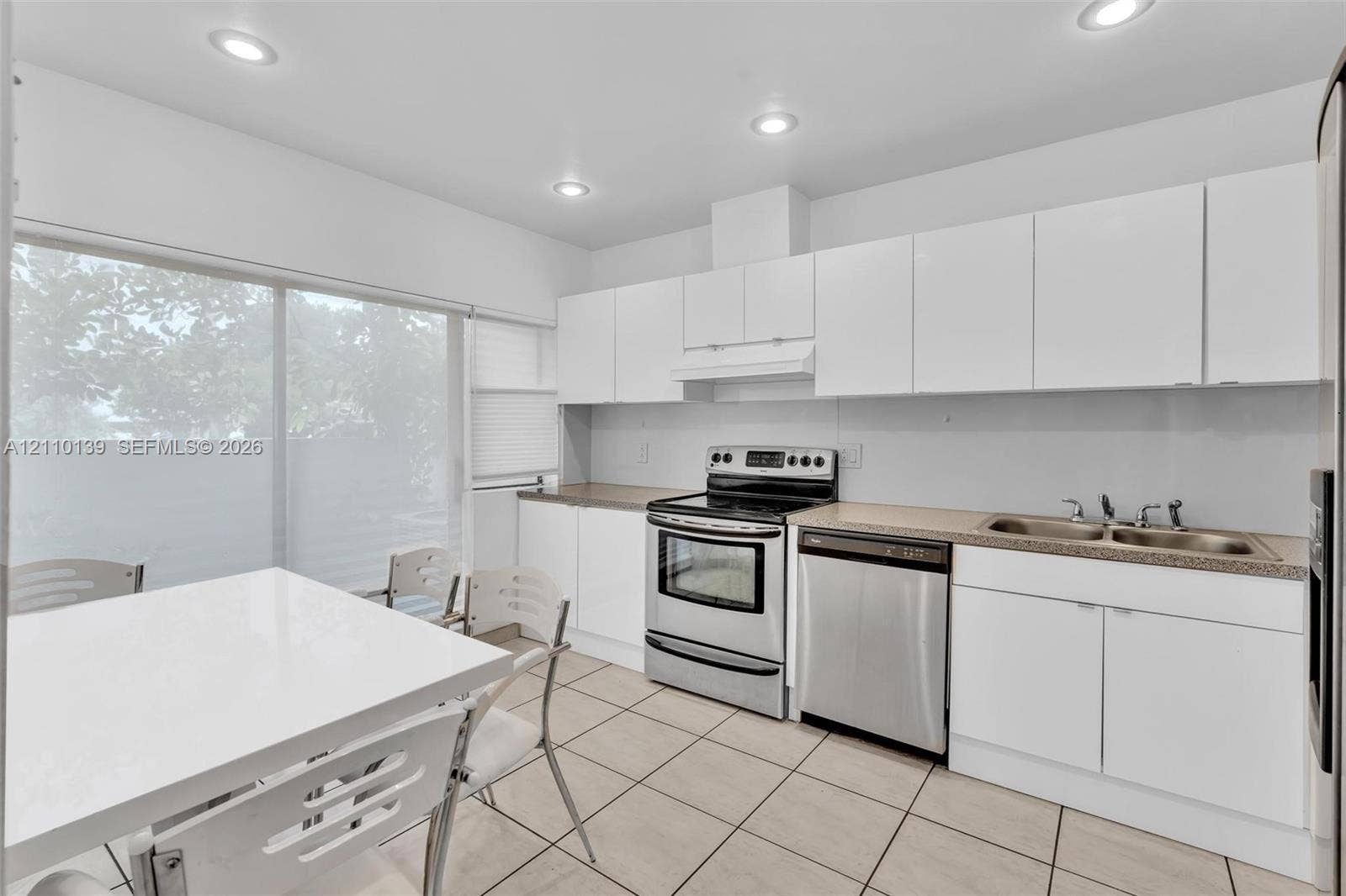 3601 NE 168th Street, #108, North Miami Beach, FL 33160 Kitchen featuring white flat-panel cabinetry, stainless steel appliances, neutral countertops, tile flooring, and recessed lighting