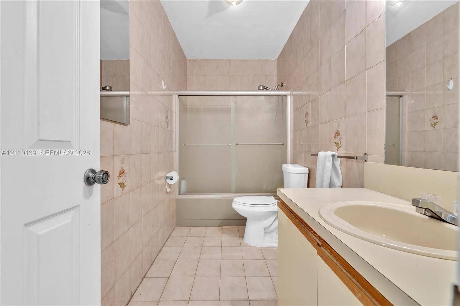 3601 NE 168th Street, #108, North Miami Beach, FL 33160 Bathroom featuring full-height wall tiling, a combination tub and shower enclosure with sliding glass doors, a vanity with a countertop-integrated basin, and large-format floor tiling