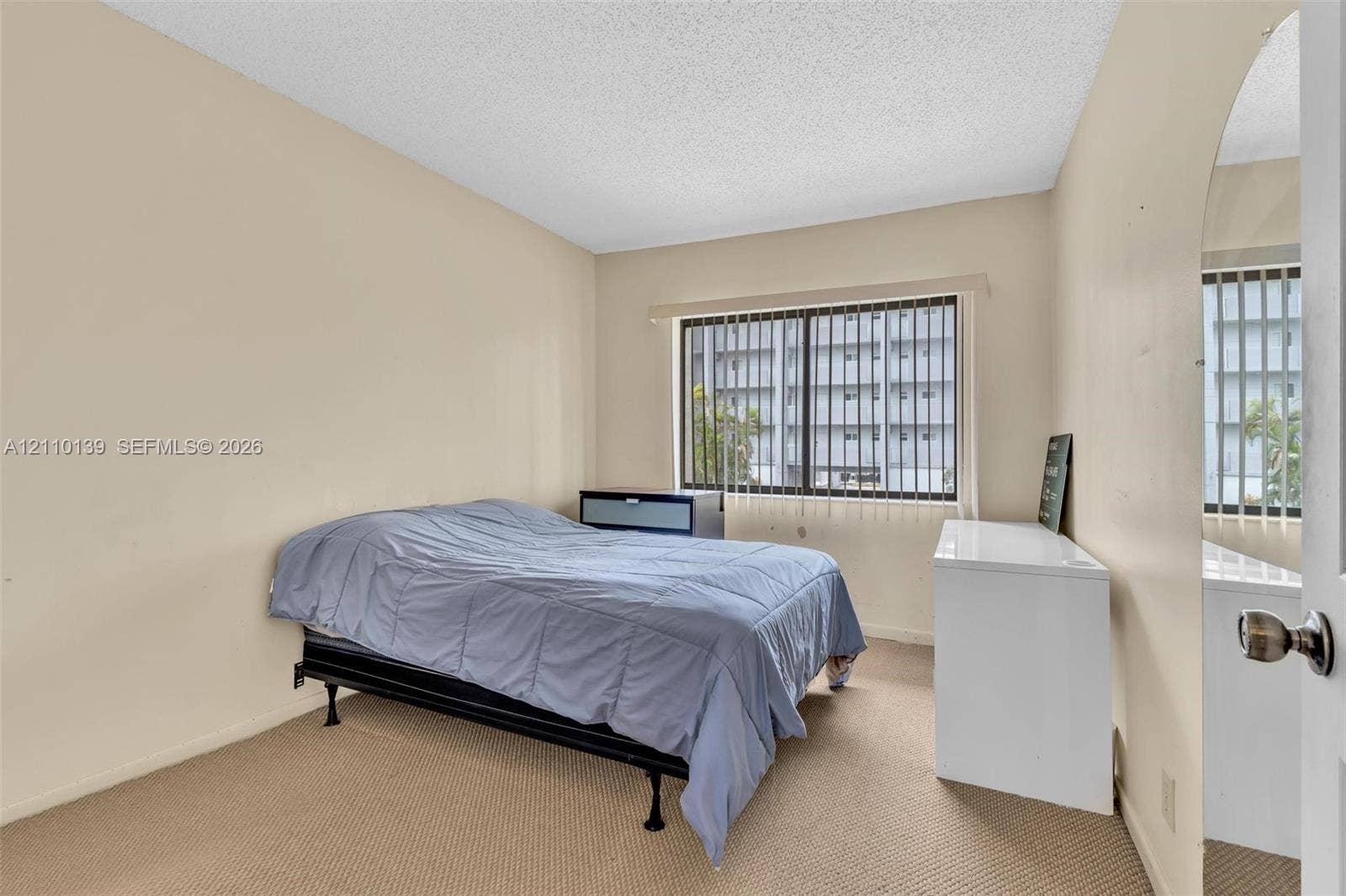 3601 NE 168th Street, #108, North Miami Beach, FL 33160 Neutral-toned interior space featuring carpeting, a multi-pane sliding window with vertical blinds, and a mirrored door