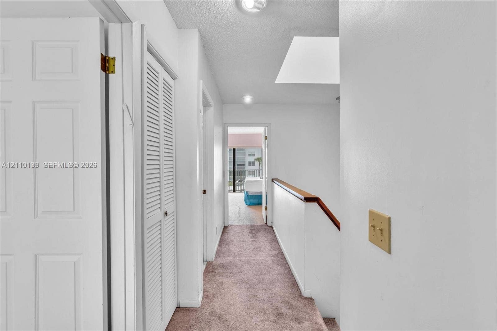 3601 NE 168th Street, #108, North Miami Beach, FL 33160 Interior hallway featuring carpeted flooring, a skylight, multi-panel doors, louvered-style closet doors, and a staircase with a wooden handrail