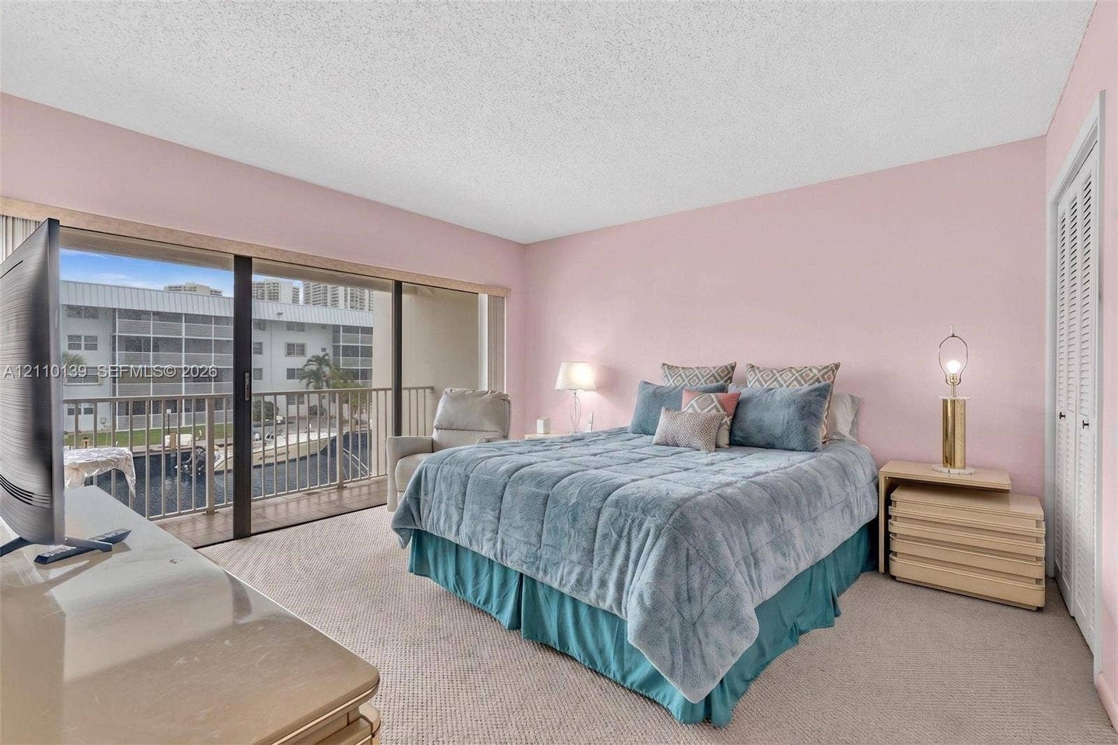 3601 NE 168th Street, #108, North Miami Beach, FL 33160 Sliding glass door opening to a private balcony with metal railing, carpeted flooring, and louvered closet doors