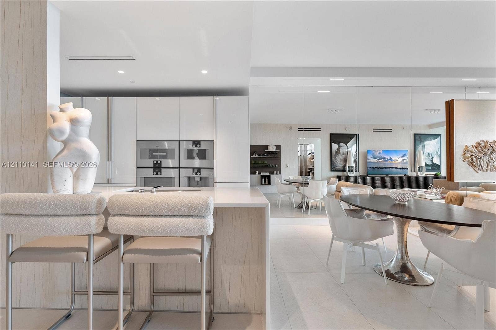 10203 Collins Avenue, #303, Bal Harbour, FL 33154 Modern kitchen featuring high-gloss cabinetry, stone-surface waterfall island, built-in dual stainless steel oven- microwave- integrated coffe sysstem for qulaity experience