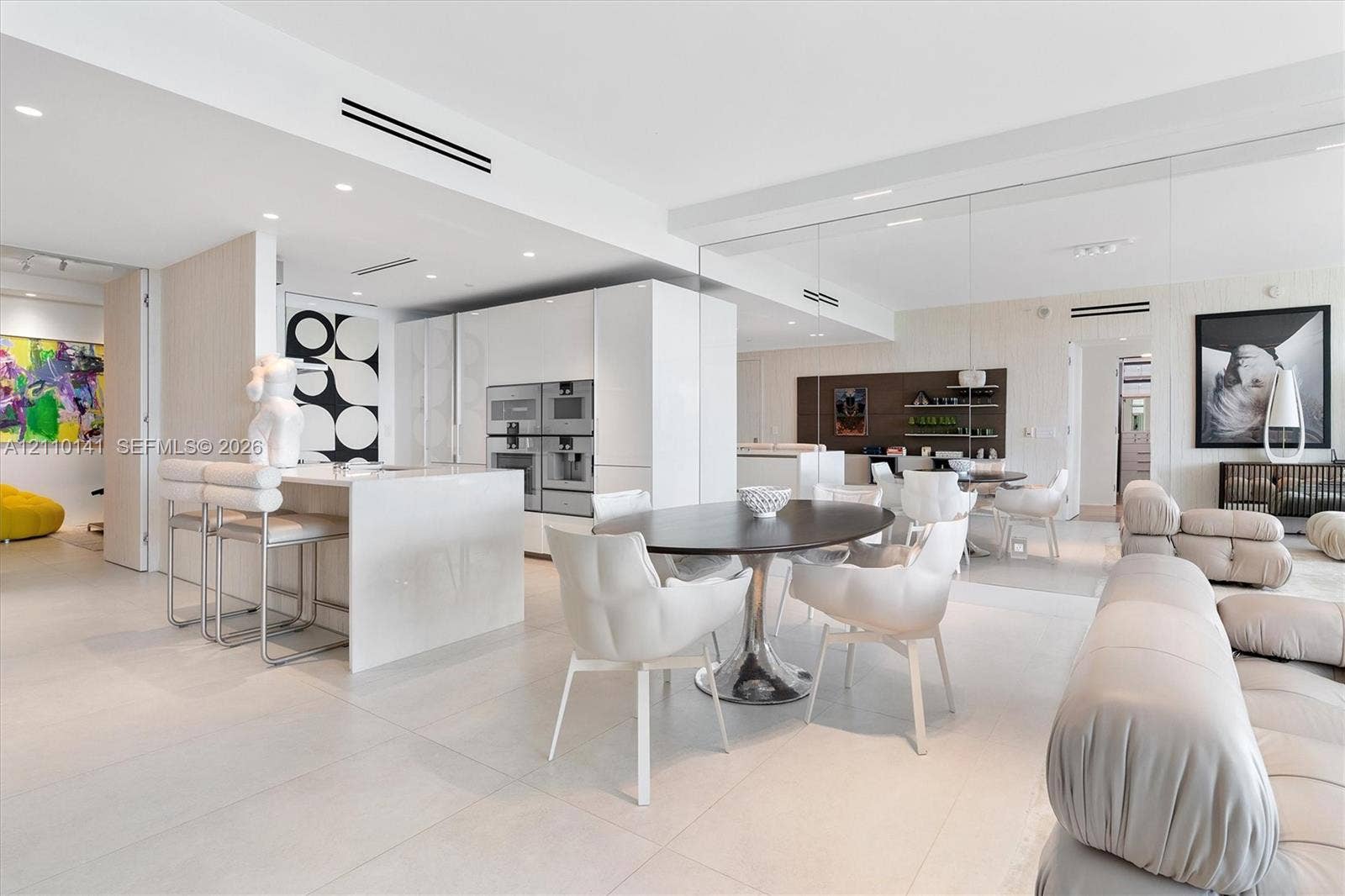 10203 Collins Avenue, #303, Bal Harbour, FL 33154 Contemporary interior featuring large-format tile flooring, high-gloss flat-panel cabinetry, a waterfall-edge kitchen island, integrated stainless steel appliances, and mirrored wall panels