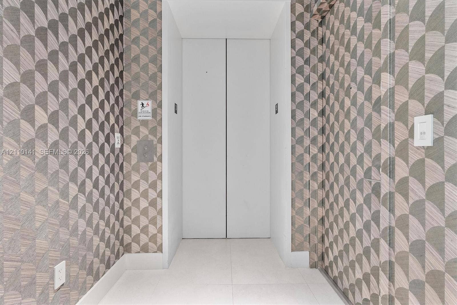 10203 Collins Avenue, #303, Bal Harbour, FL 33154 Private elevator entry featuring white double doors, geometric patterned wall covering, and neutral tile flooring
