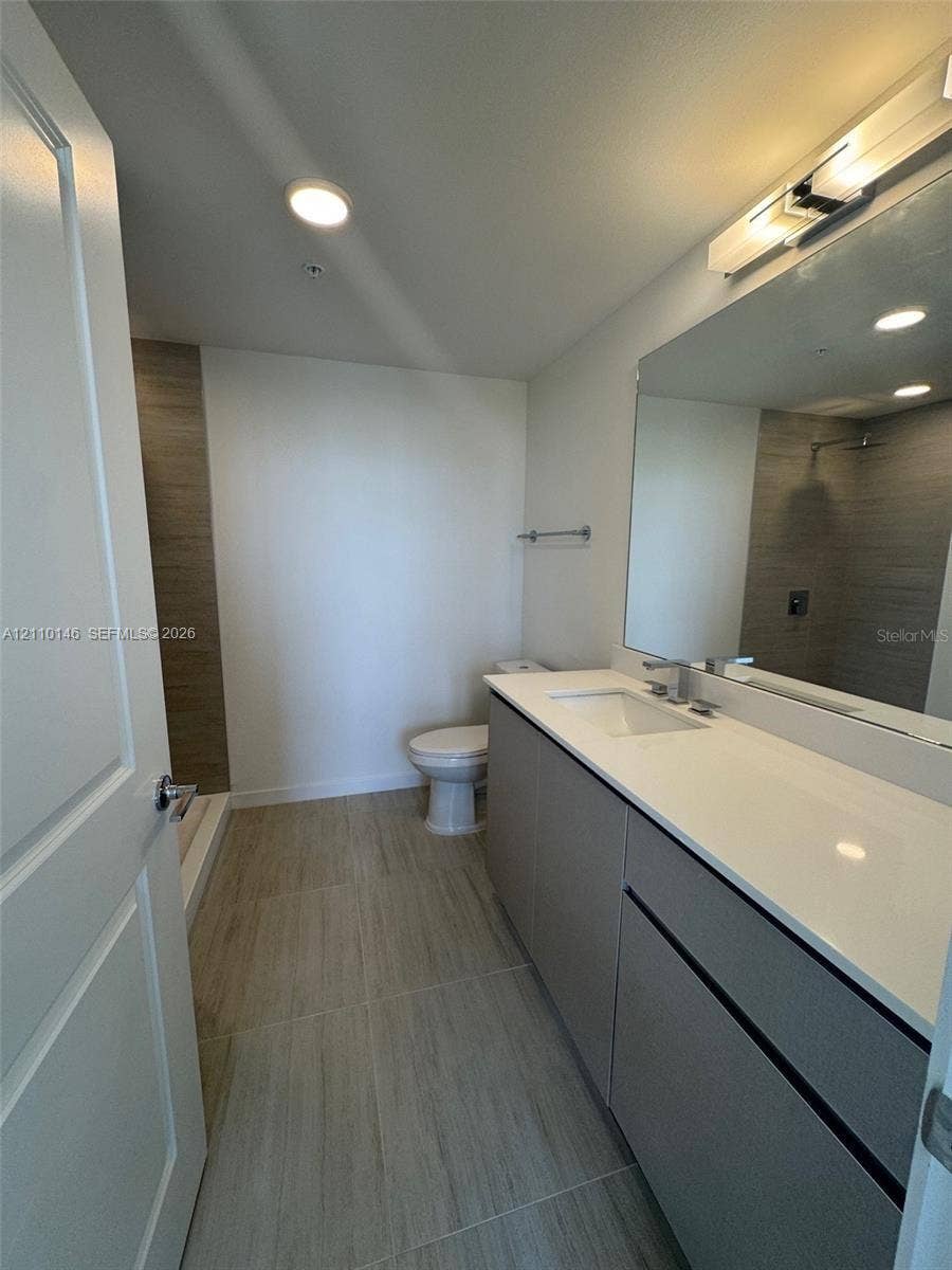 5563 Millenia Park Boulevard, #427, Orlando, Orlando, FL 32839 Bathroom featuring a floating vanity with a light-toned countertop, large wall-mounted mirror, wood-finish floor tiling, and a walk-in shower with vertical tile surround