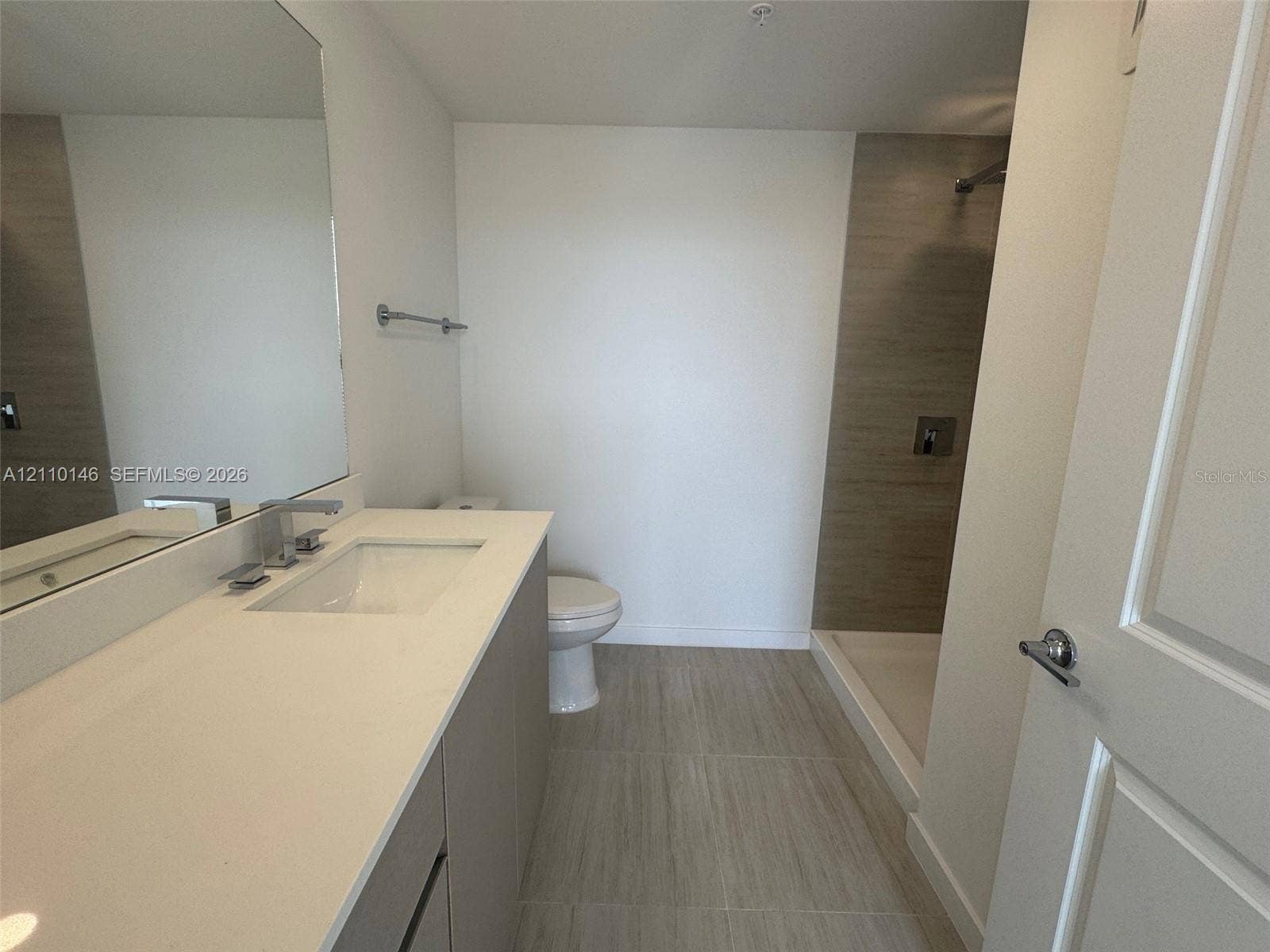 5563 Millenia Park Boulevard, #427, Orlando, Orlando, FL 32839 Bathroom featuring a vanity with a white countertop and rectangular sink, large wall-mounted mirror, walk-in shower with neutral tile surround, and tile flooring