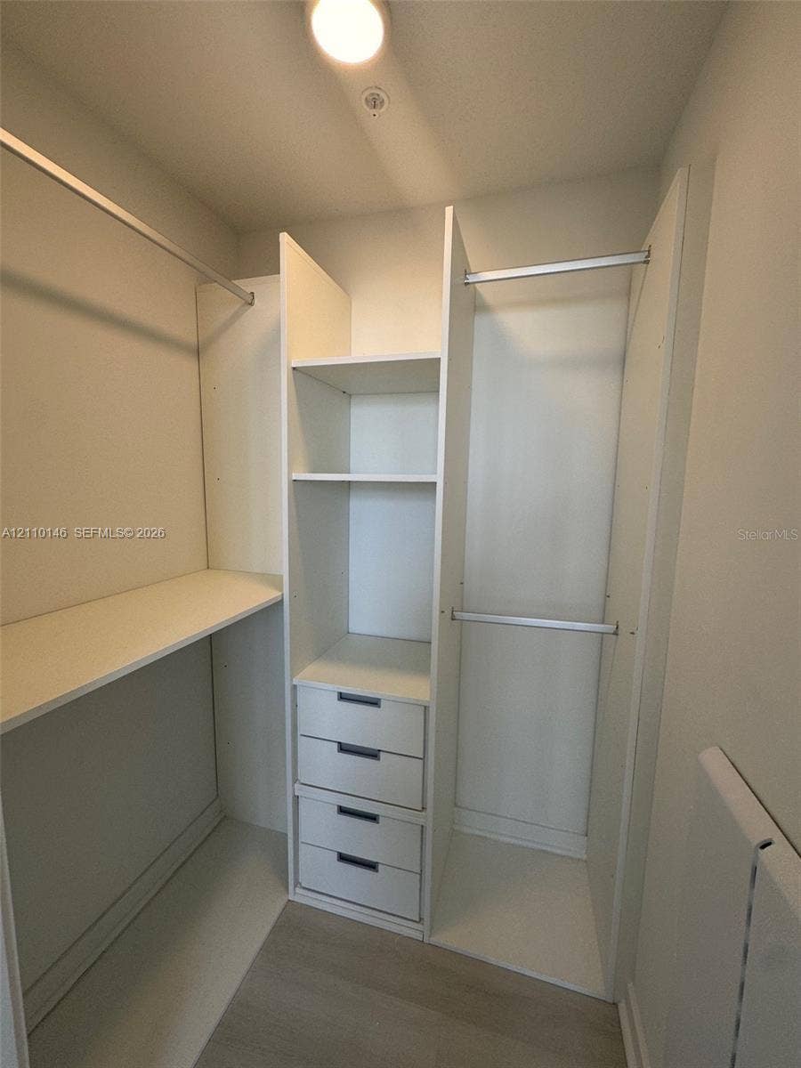 5563 Millenia Park Boulevard, #427, Orlando, Orlando, FL 32839 Walk-in closet featuring white built-in shelving, integrated storage drawers with matte finish hardware, dual-level hanging rods, and wood-finish flooring