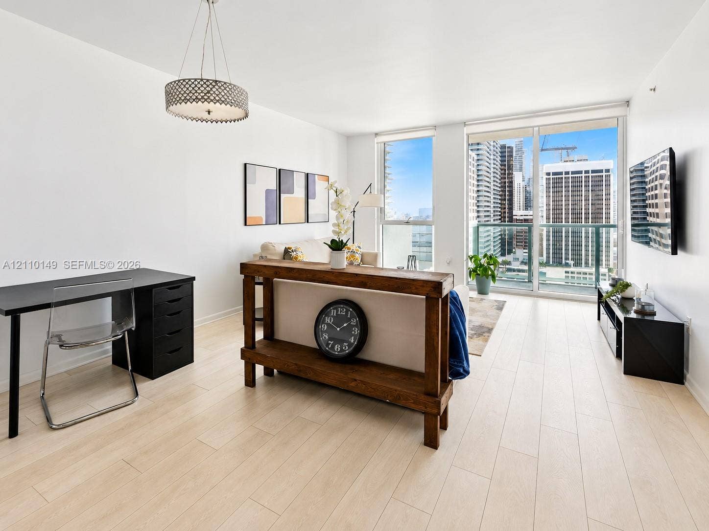 Light-toned wood-finish flooring, floor-to-ceiling windows, glass-panel balcony door, and a circular drum pendant light fixture