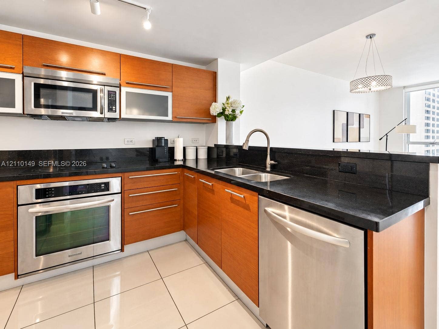Kitchen featuring wood-finish cabinetry, dark stone countertops, stainless steel appliances, dual-basin sink, and tile flooring