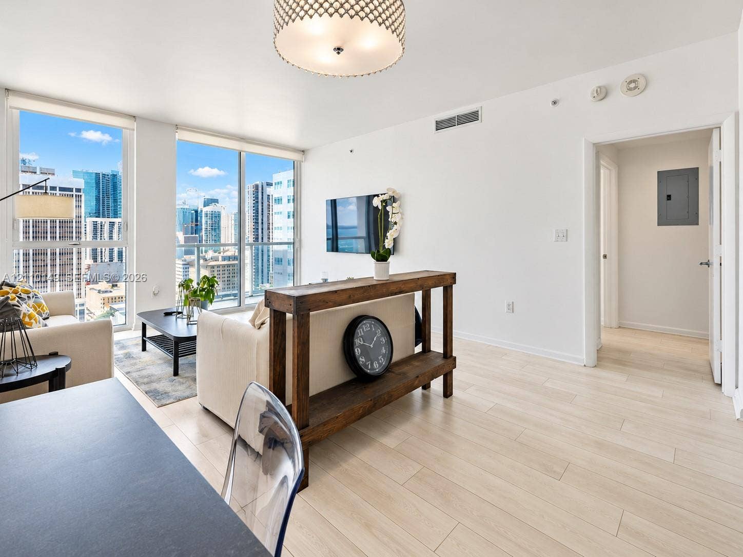 Floor-to-ceiling windows, wood-finish flooring, patterned drum pendant lighting, and urban skyline backdrop