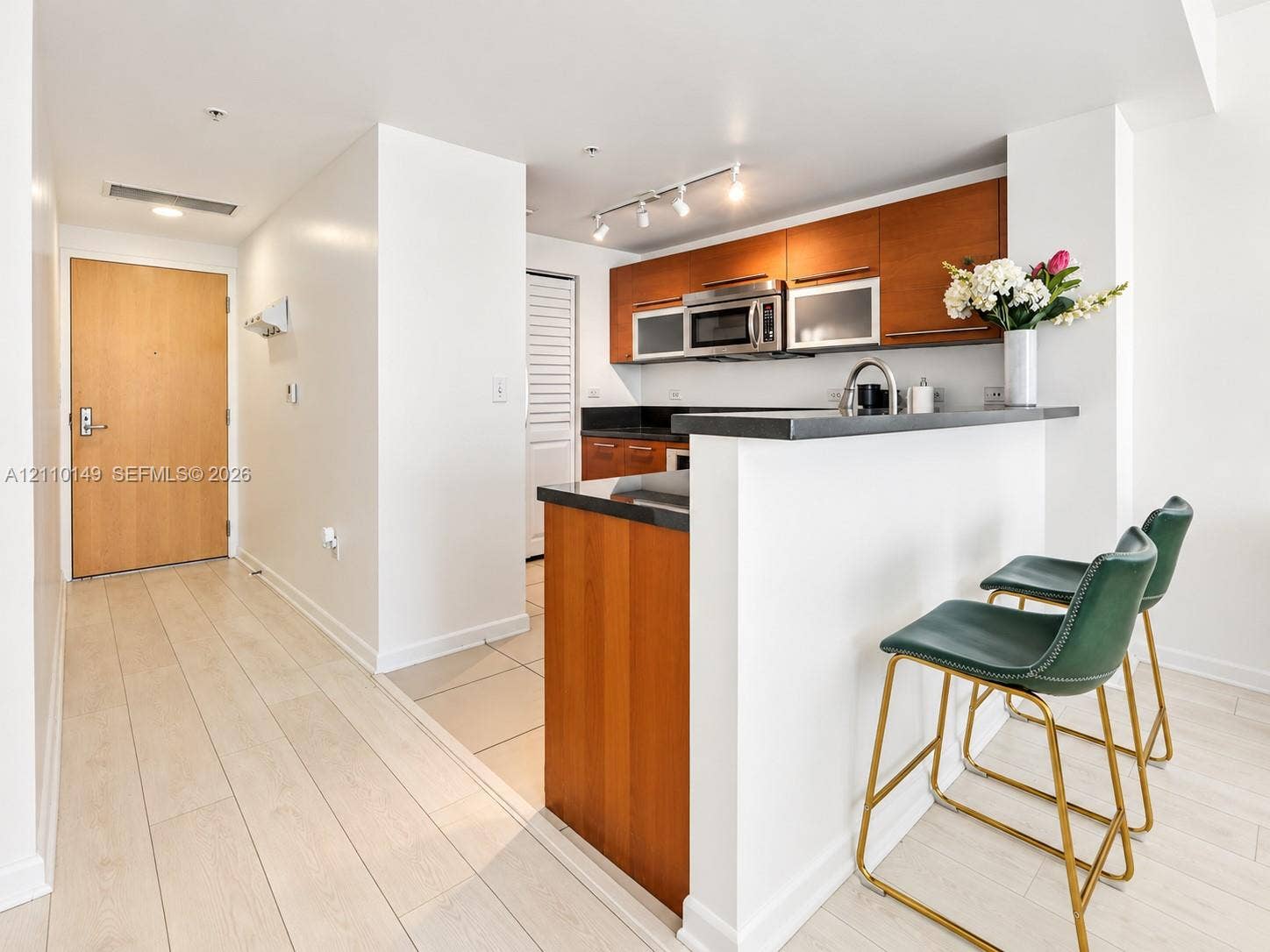 Kitchen featuring wood-finish cabinetry, dark stone countertops, stainless steel appliances, and a breakfast bar with track lighting