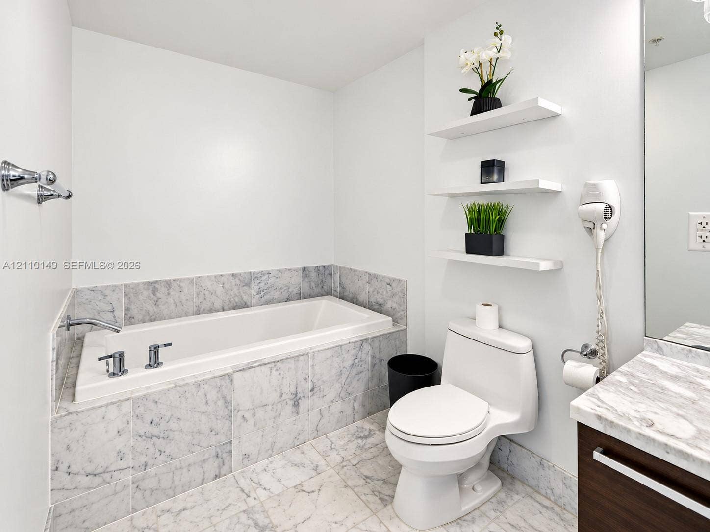 Bathroom featuring a stone-surround soaking tub, stone tile flooring, a vanity with a stone countertop, and three integrated wall-mounted shelves