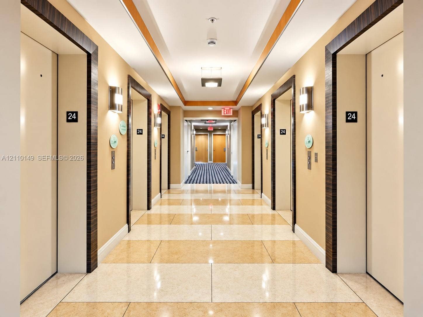 Hallway featuring high-gloss polished stone tile flooring, recessed ceiling lighting with wood-toned trim, and modern wall-mounted light fixtures