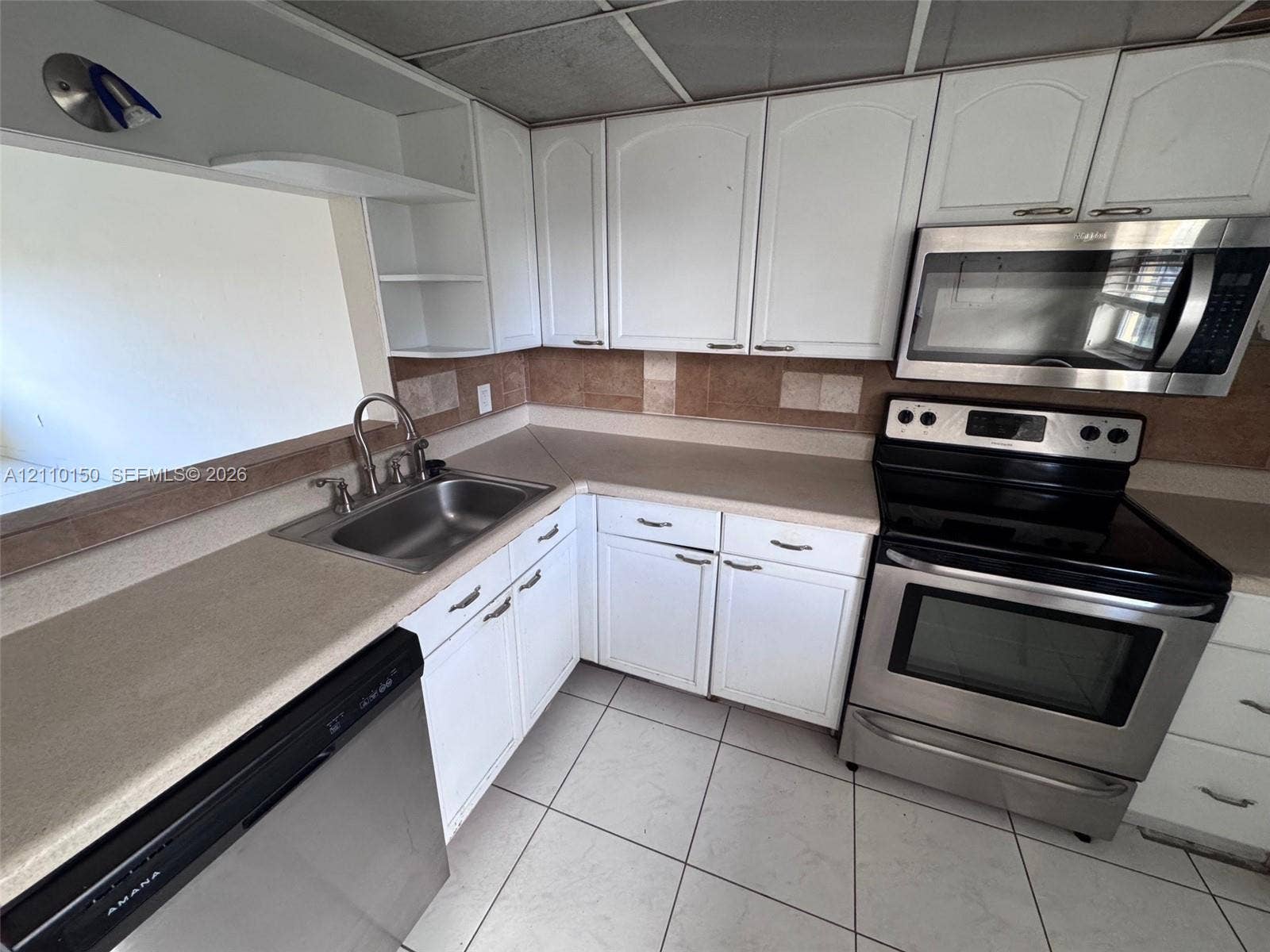 20111 NE 27th Court, #K212, Aventura, Aventura, FL 33180 Kitchen featuring white cabinetry, stainless steel appliances, neutral countertops, tile backsplash, and tile flooring