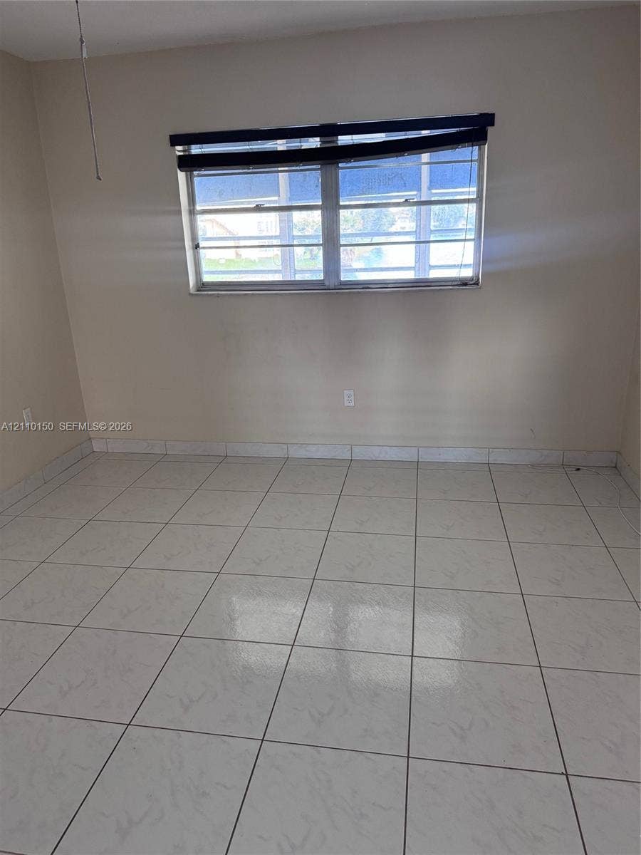 20111 NE 27th Court, #K212, Aventura, Aventura, FL 33180 Interior space featuring neutral wall paint, white tile flooring, and a multi-pane window with a horizontal window covering