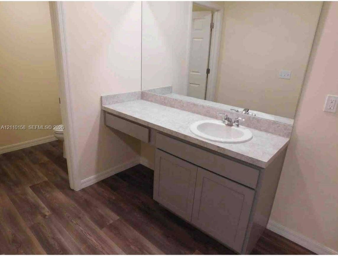 1743 SW Bellevue Avenue, Port St Lucie, FL 34953 Vanity featuring a light-toned countertop, integrated basin, dual-handle faucet, grey cabinetry, and wood-finish flooring