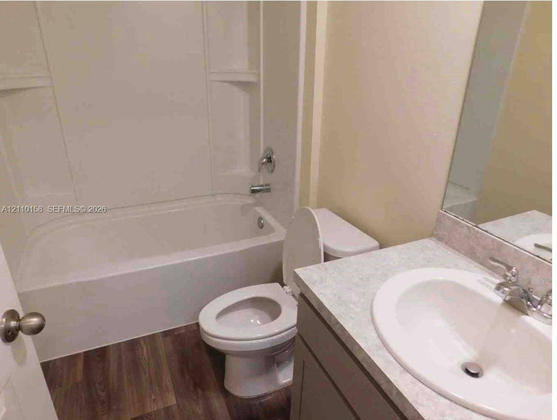 1743 SW Bellevue Avenue, Port St Lucie, FL 34953 Bathroom featuring a vanity with a stone-finish countertop, integrated sink, wood-finish flooring, and a tub-shower combination with a surround