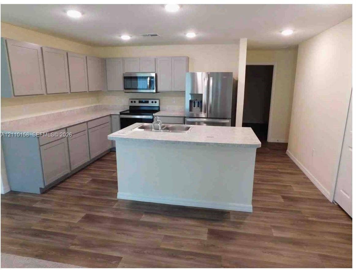 1743 SW Bellevue Avenue, Port St Lucie, FL 34953 Kitchen featuring light-toned cabinetry, stone-finish countertops, stainless steel appliances, a center island with a dual-basin sink, and wood-finish flooring