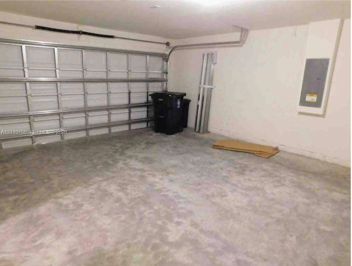 1743 SW Bellevue Avenue, Port St Lucie, FL 34953 Enclosed garage space featuring a metal sectional overhead door, finished concrete flooring, and an integrated electrical service panel